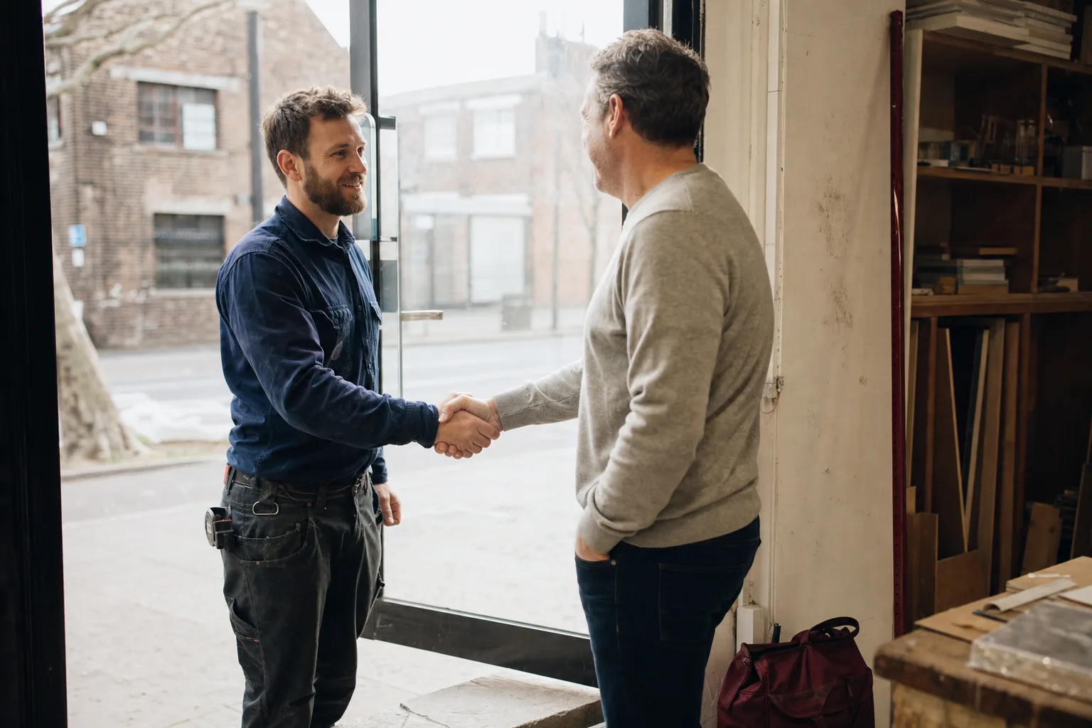 A contractor shaking hands with a business owner in a workshop doorway
